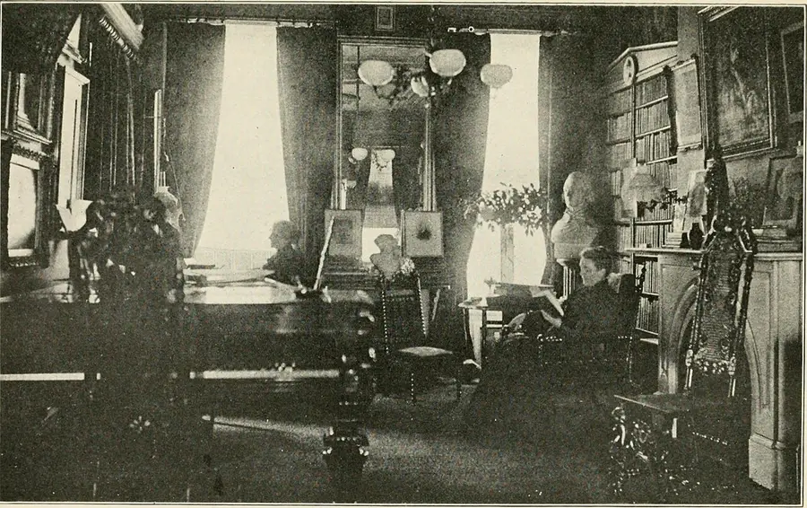 A dim, book-lined library with tall curtained windows. A woman sits by the far window; another, at right, reads in an armchair beside a bust and a carved chair.