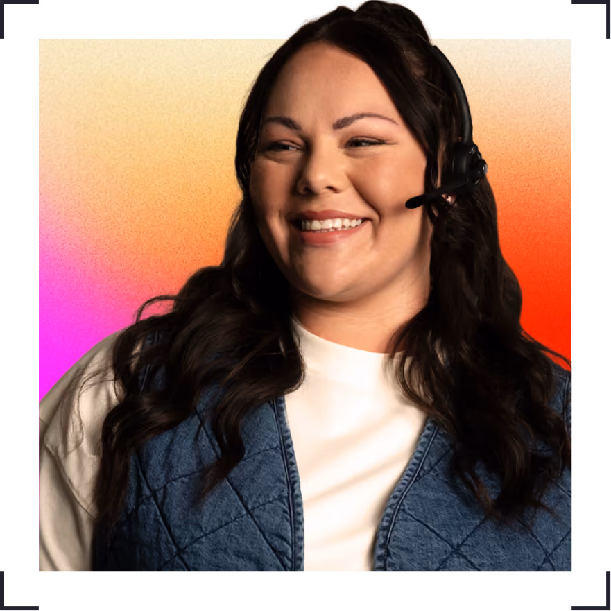 Smiling woman with dark hair wearing a headset and blue quilted vest over a white top.