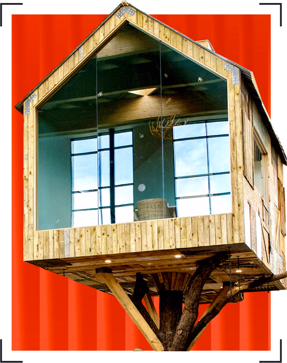 Moneypenny HQ treehouse with large glass windows showing interior chair and antler chandelier.