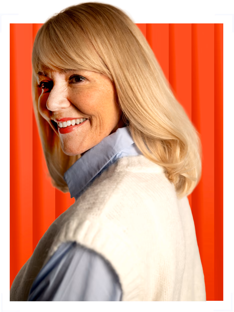 Smiling woman with blonde hair wearing a white sweater and blue shirt over an orange and red background.