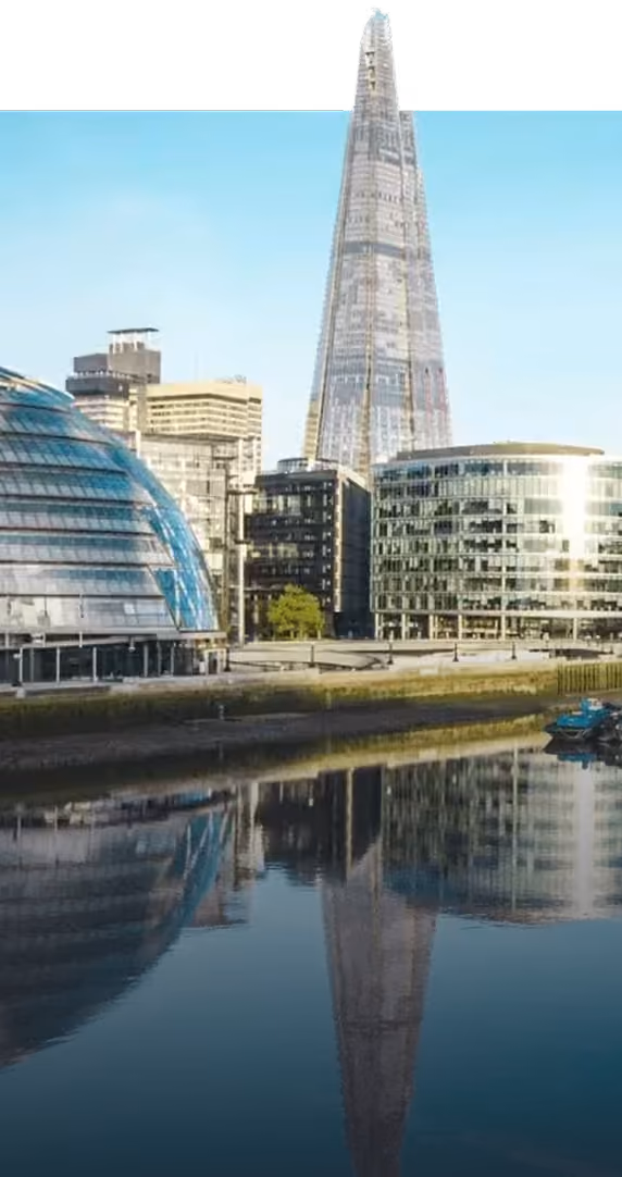 The Shard skyscraper and surrounding modern buildings reflected in a river under a clear sky.