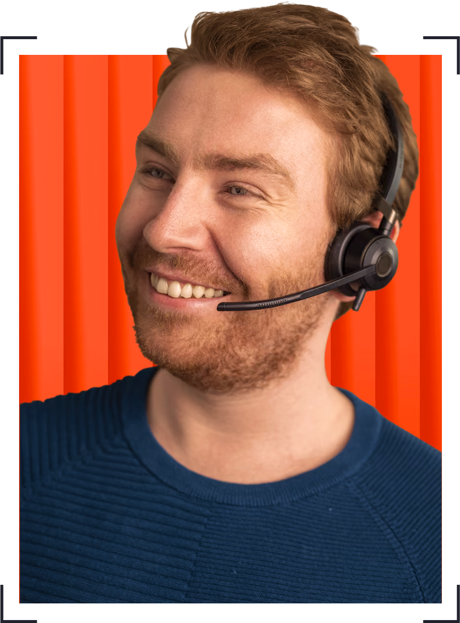 Smiling man with short hair wearing a headset and blue sweater against a red background.
