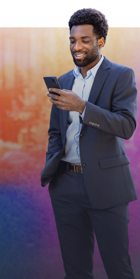 Smiling man in a dark suit looking at his smartphone with one hand in pocket.