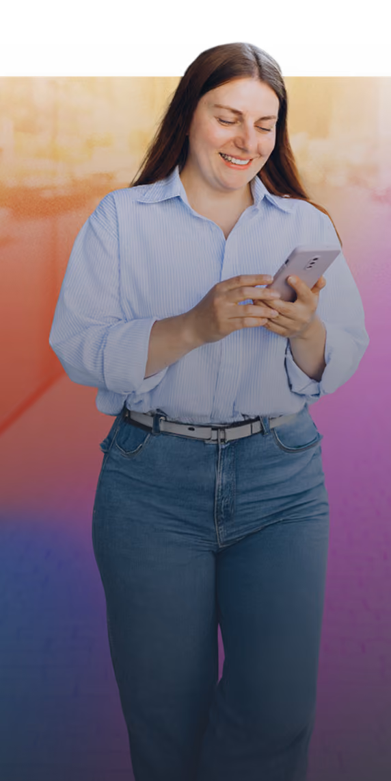 Smiling woman in blue shirt and jeans looking at her mobile phone against a colorful background.