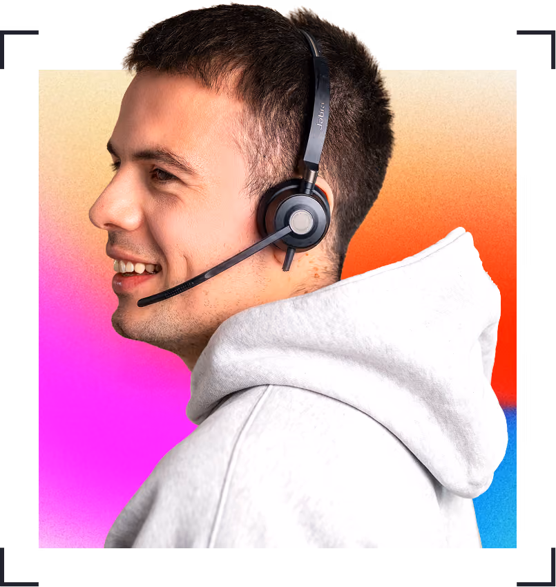 Smiling man wearing a grey hoodie and black headset with microphone on a colorful gradient background.