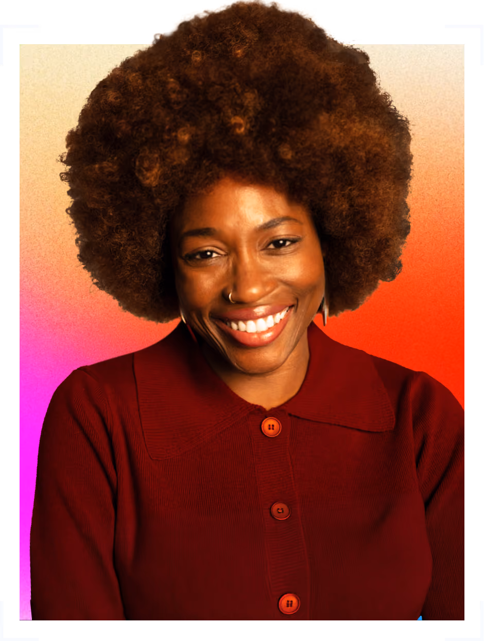 Smiling woman with large curly afro hairstyle wearing a red buttoned sweater against a gradient background.