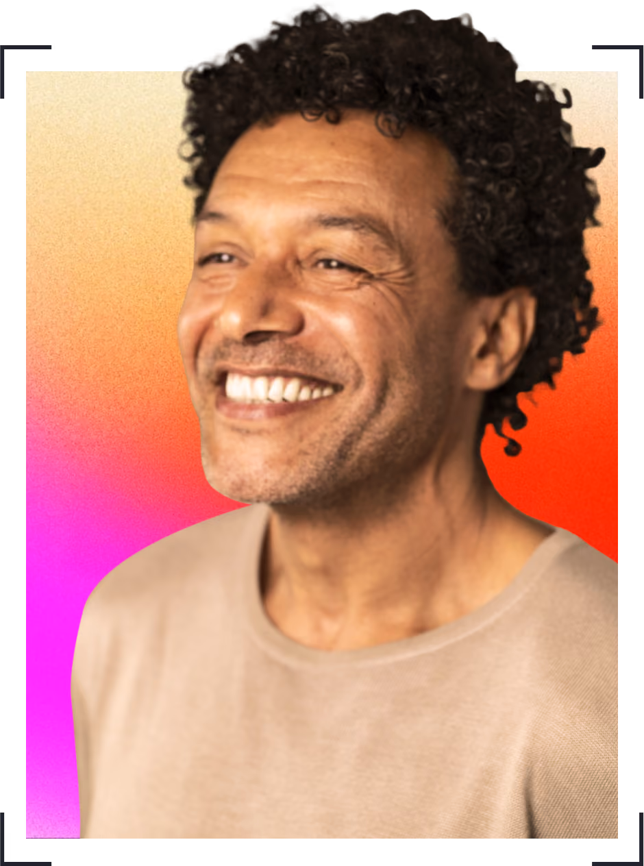Smiling man with curly hair wearing a beige jumper against a gradient background.