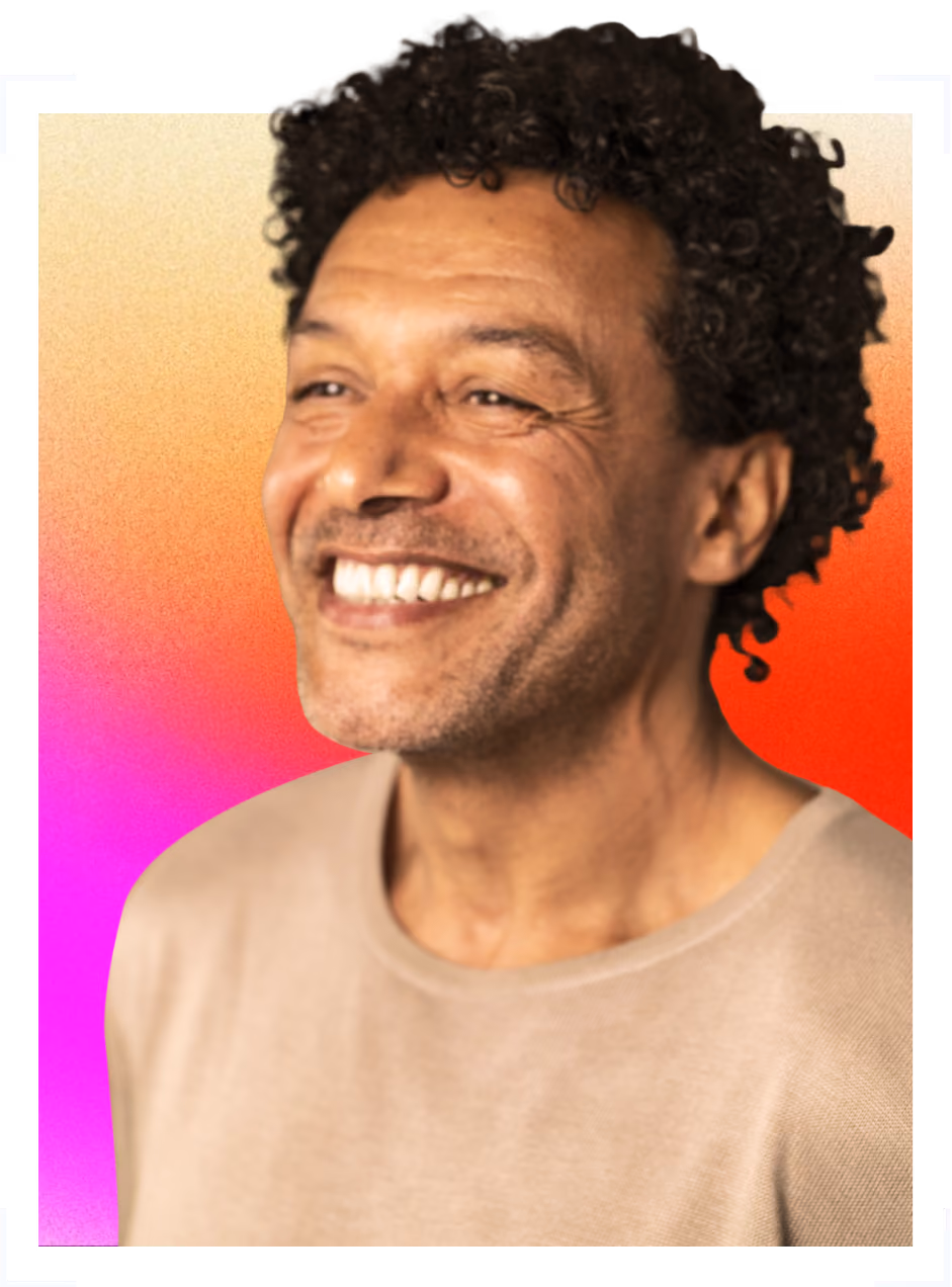 Smiling man with curly hair wearing a beige top against a vibrant pink, orange, and red background.