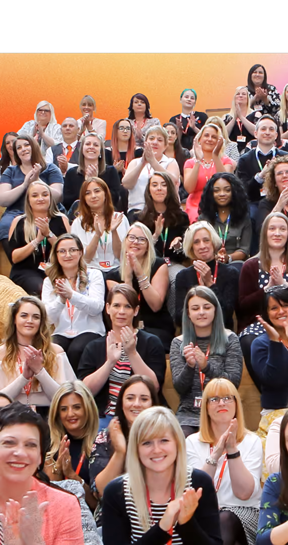 Large diverse group of people seated and clapping, smiling in front of an orange gradient background.