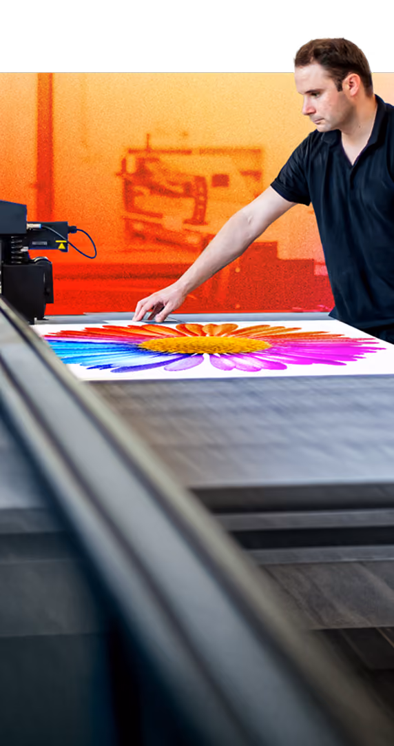 Man in black shirt inspecting vibrant, multi-coloured flower print on large flatbed printer.