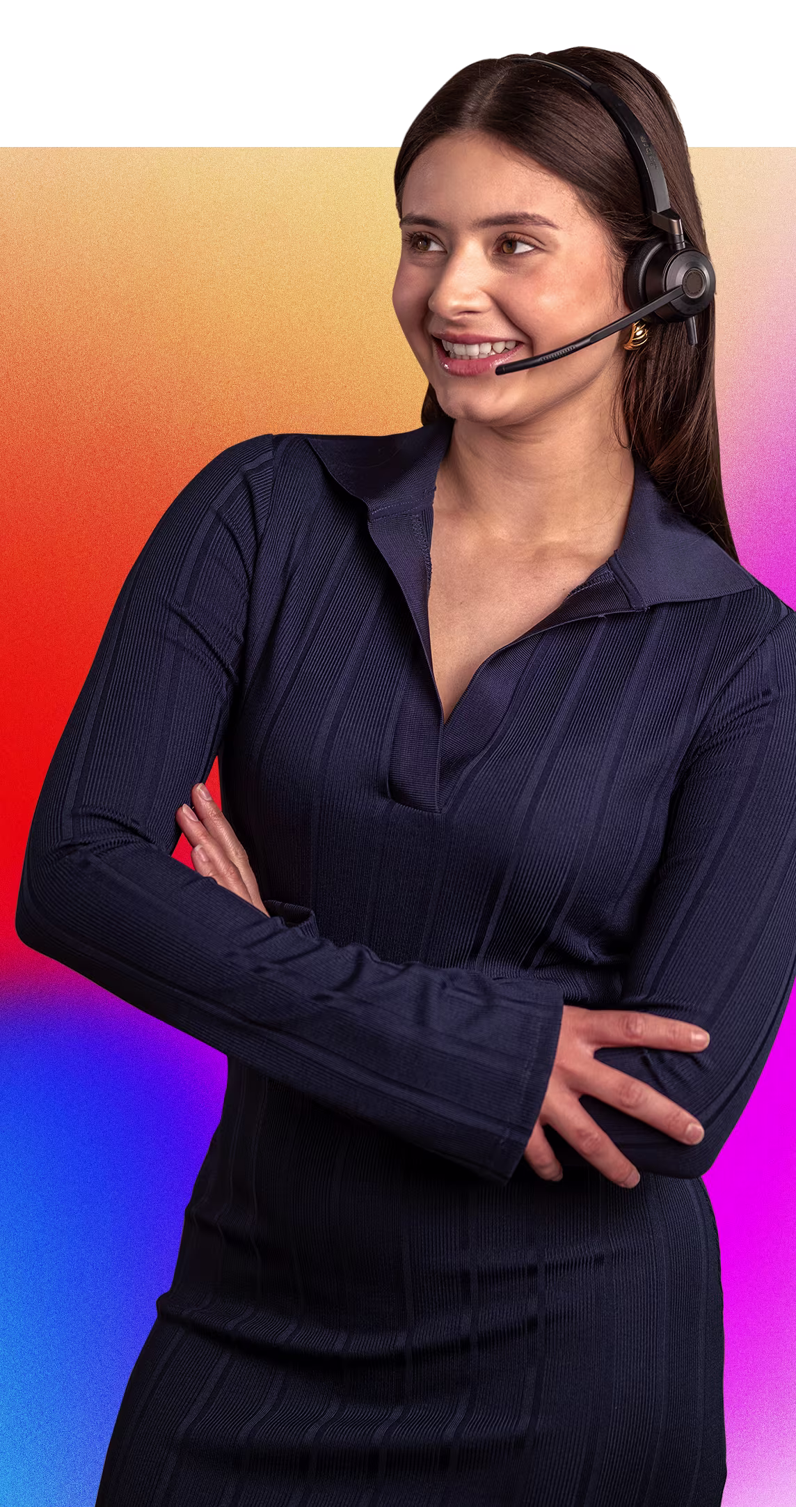 Young woman with brown hair smiles wearing a navy dress and headset with arms crossed.