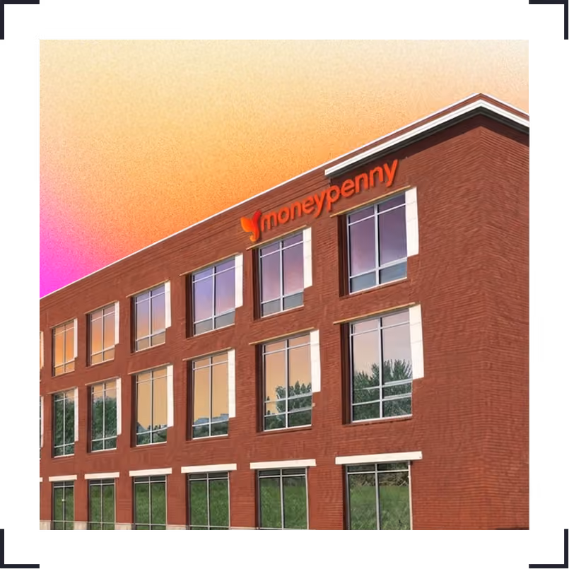 Three-storey red brick office building with large windows reflecting trees and sky, with an orange 'moneypenny' sign at the top corner against a gradient orange and purple sky.