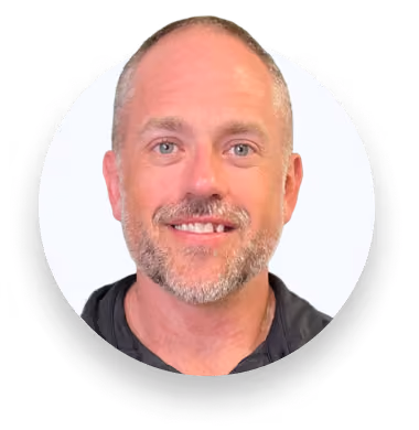 Portrait of a smiling middle-aged man with short grey hair, a trimmed beard, and blue eyes, wearing a black shirt against a white background.
