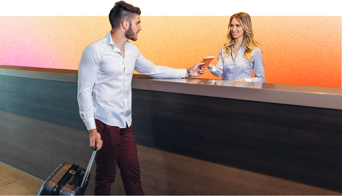 Man pulling a suitcase hands a passport to a smiling hotel receptionist behind a modern front desk with a warm gradient background.