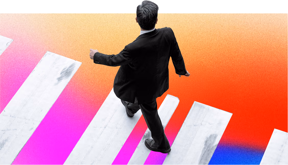 Man in a black suit walking across a white pedestrian crossing on a gradient background that transitions from orange to pink to blue.