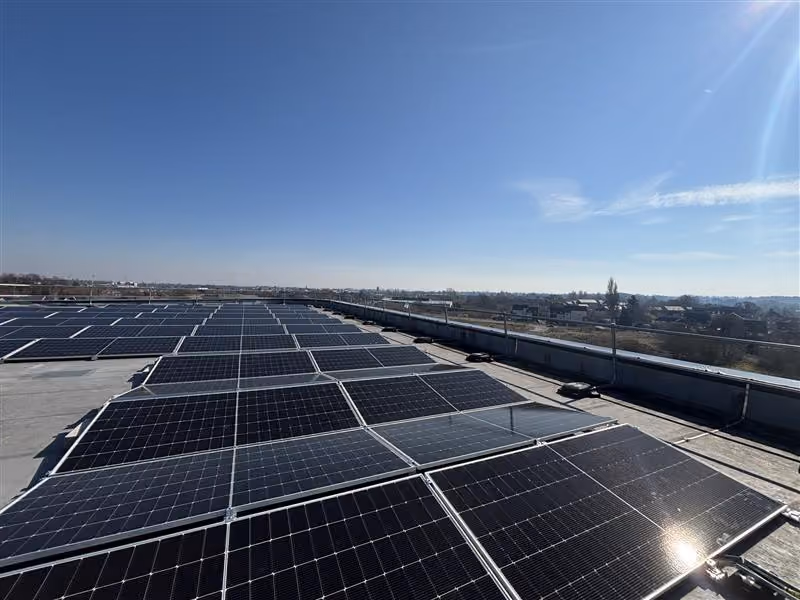 Rows of solar panels installed on a flat rooftop under a clear blue sky with sunlight.