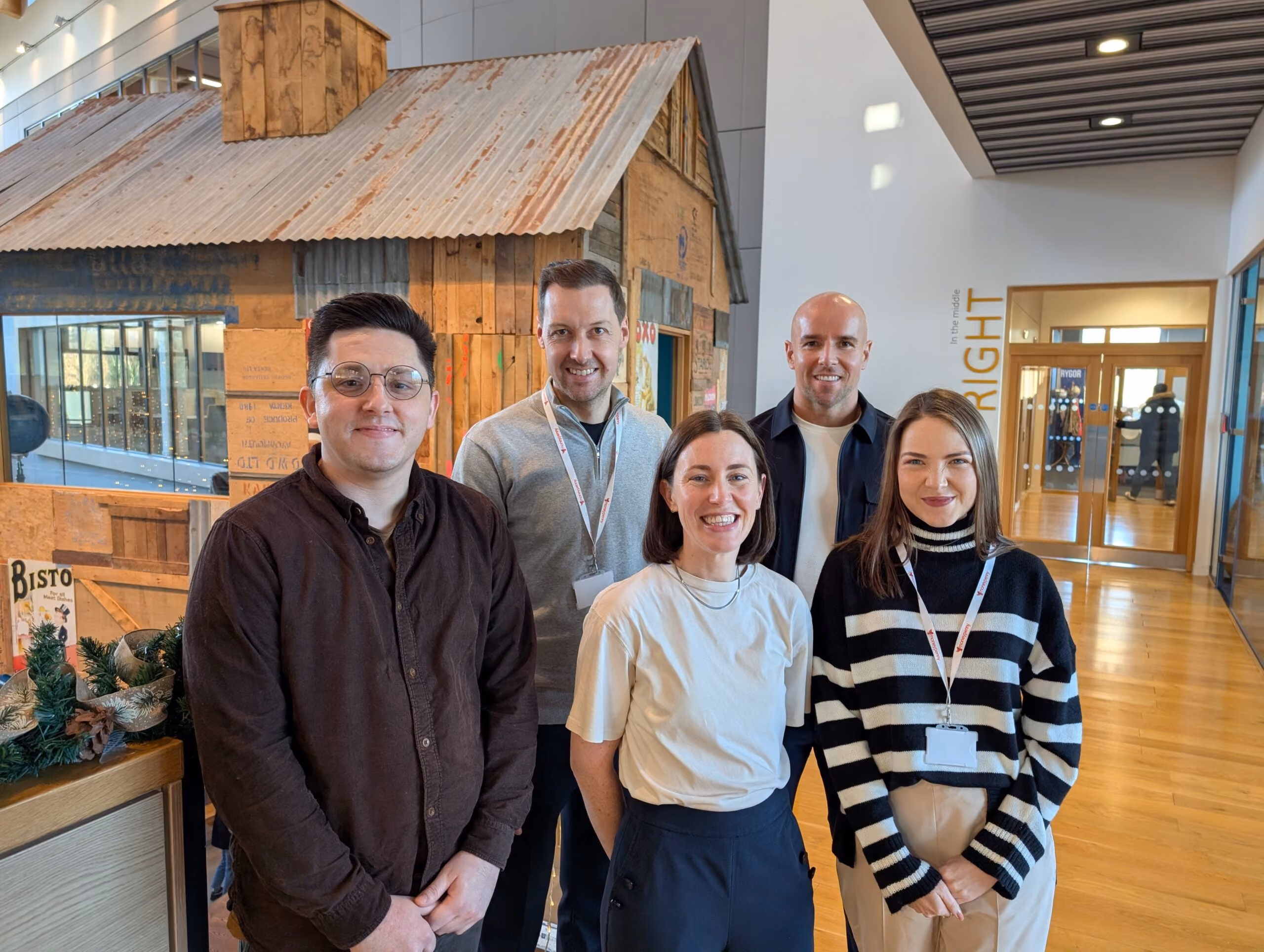 Group of five people smiling indoors with a rustic wooden structure and office background.