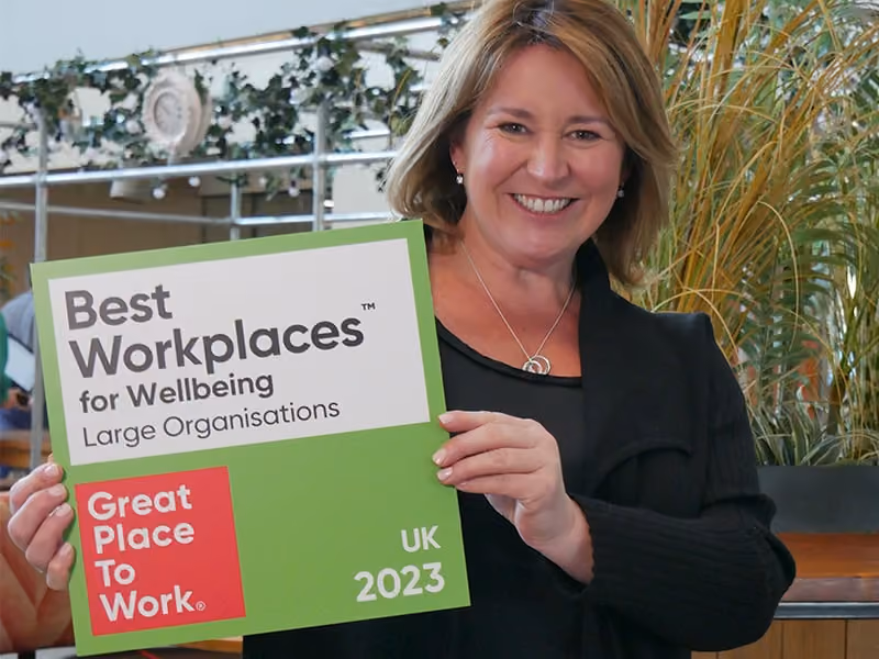 Smiling woman holding a 'Best Workplaces for Wellbeing Large Organisations UK 2023' award plaque.