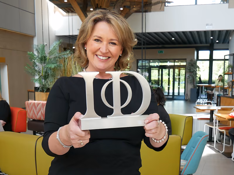 Smiling woman in black holding a silver IOD award in a bright modern lounge area.
