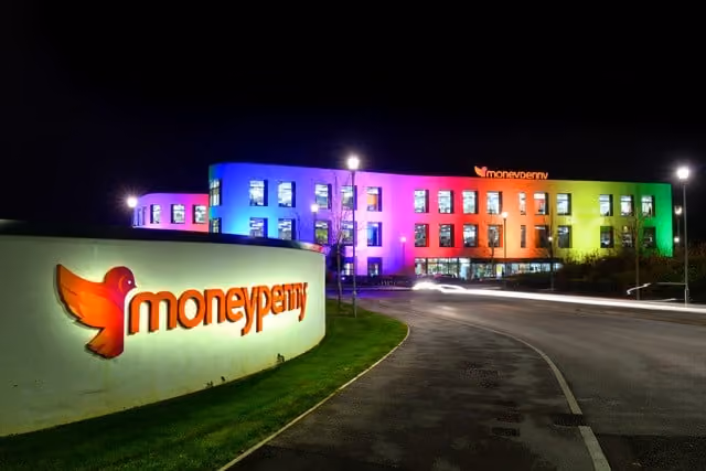 Moneypenny office building lit with rainbow-colored lights at night beside a lit company sign.