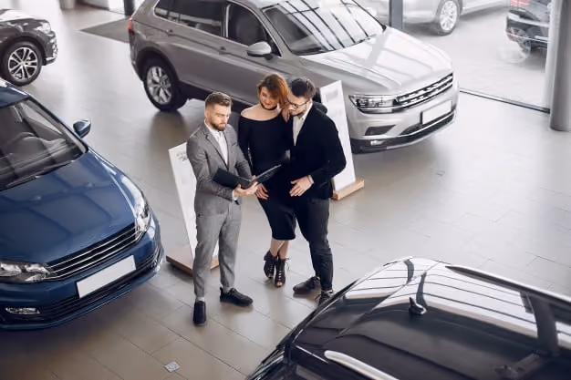 Car dealer in gray suit showing a folder to a couple inside a modern car showroom.