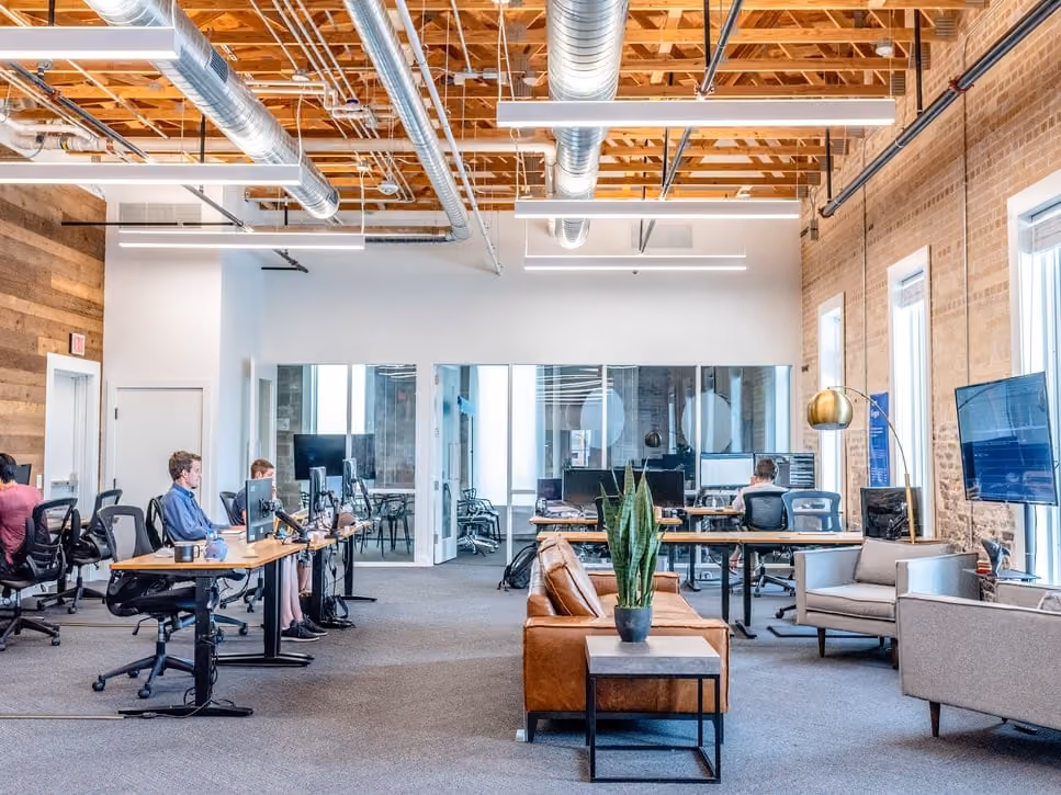 Modern office space with people working at desks and a seating area with couches and a plant.