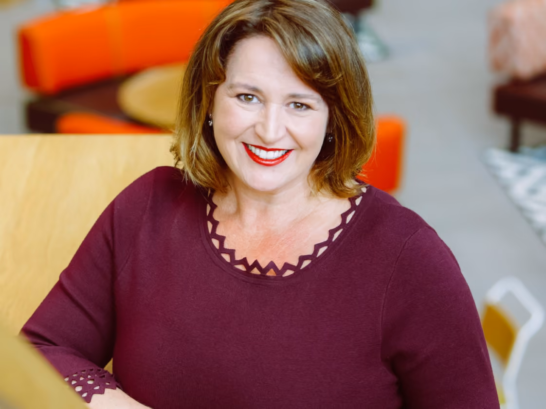 Smiling woman with shoulder-length light brown hair wearing a maroon top with patterned neckline.