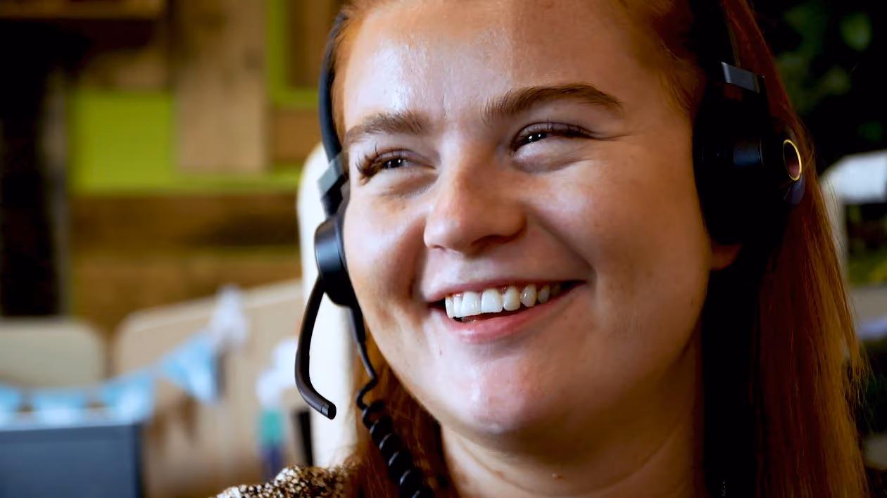 Smiling woman with red hair wearing a headset in an office setting.