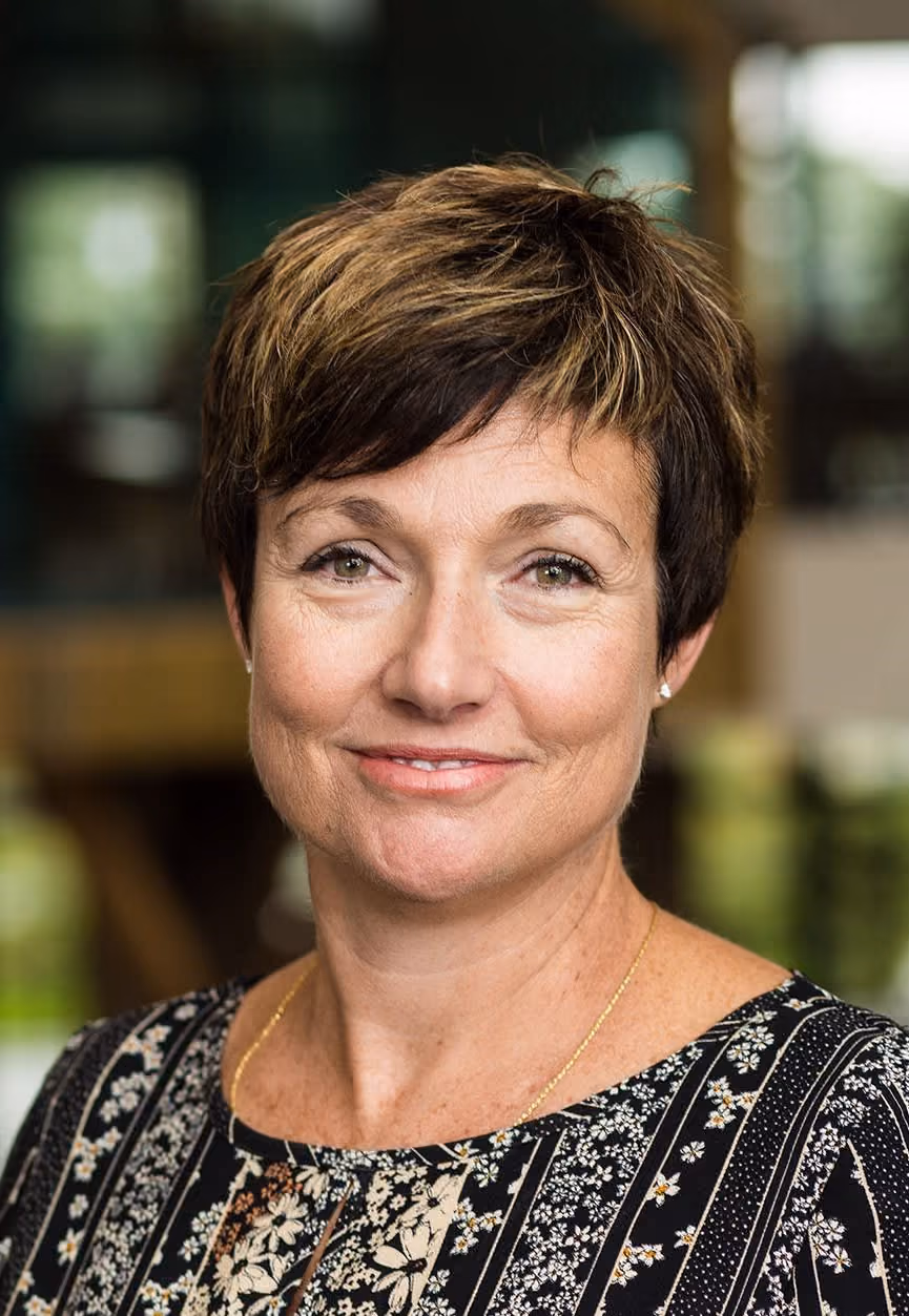 Smiling woman with short brown hair wearing a patterned blouse and gold necklace.