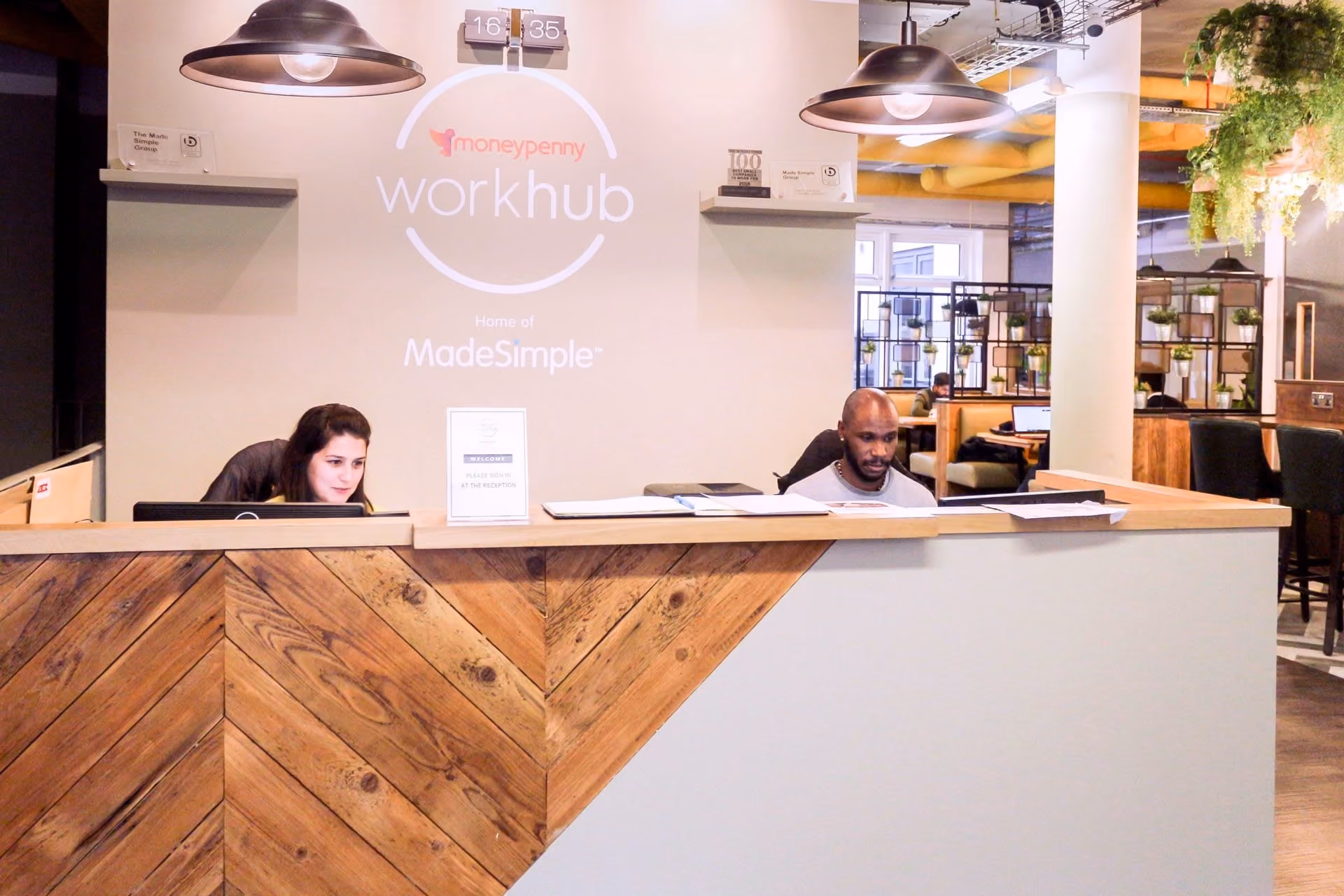 Reception area with two people working behind a wooden and white desk at the moneypenny workhub.
