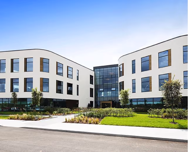 Modern three-story office building with curved walls, large windows, and landscaped front lawn.