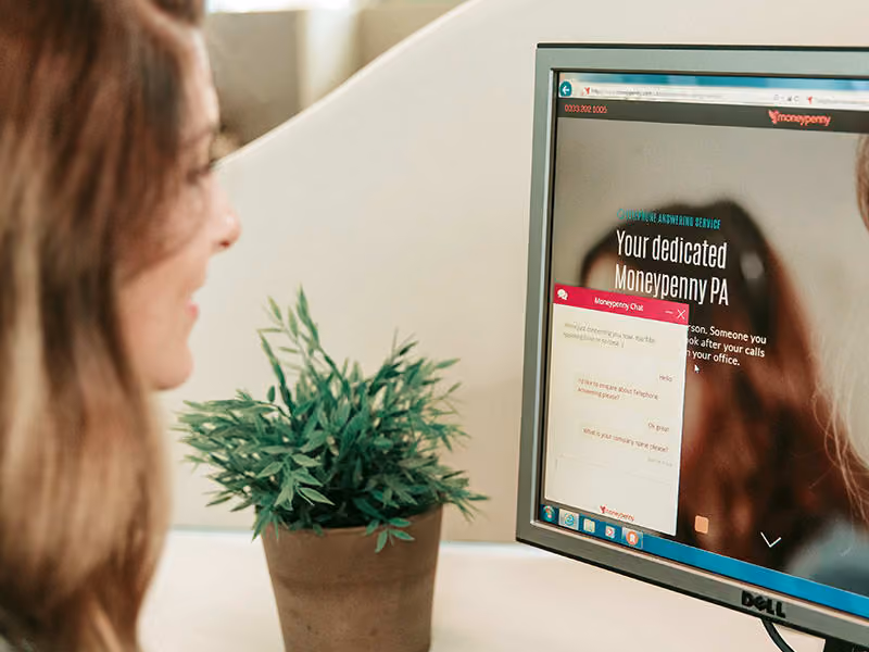 Woman looking at a computer screen displaying a Moneypenny chat window and webpage.