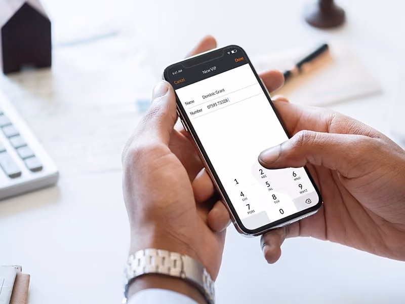 Person holding smartphone adding a new VIP contact named Dominic Grant with a phone number.
