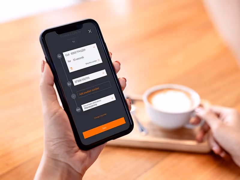 Hand holding smartphone showing call forwarding settings with a cup of coffee on a wooden table.