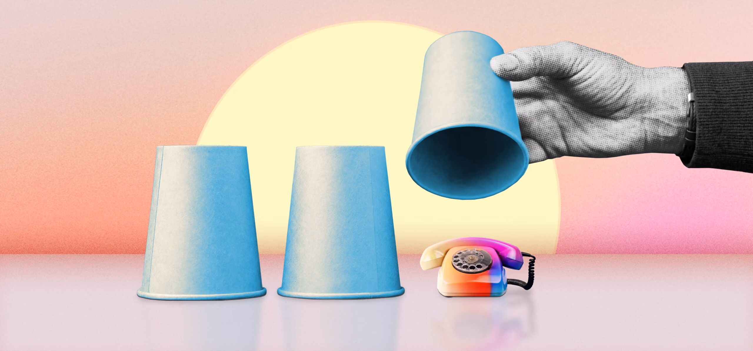 Hand lifting one of three blue cups hiding a colorful rotary phone on a pink and yellow background.