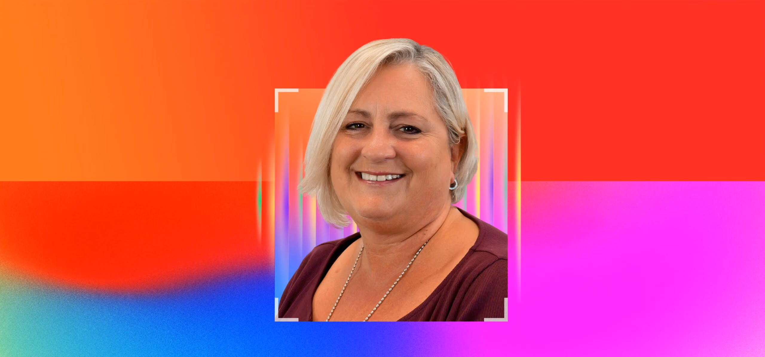 Smiling woman with short blonde hair wearing a purple top and silver necklace on a colorful background.