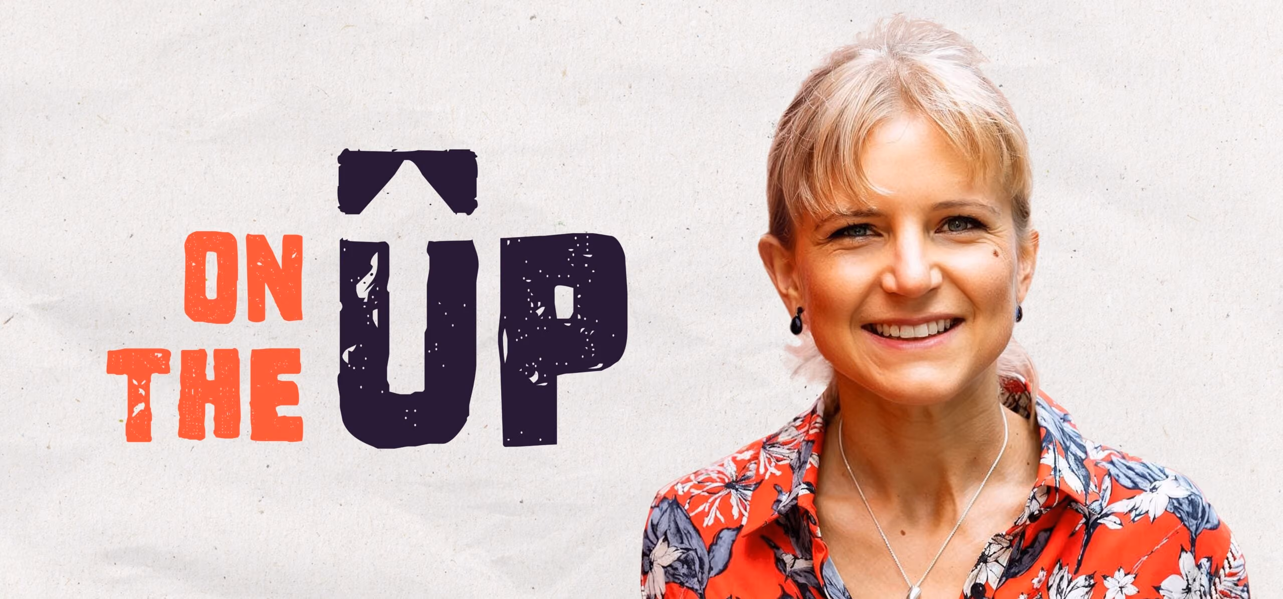 Smiling blonde woman wearing a red floral shirt with a silver necklace against a plain background.