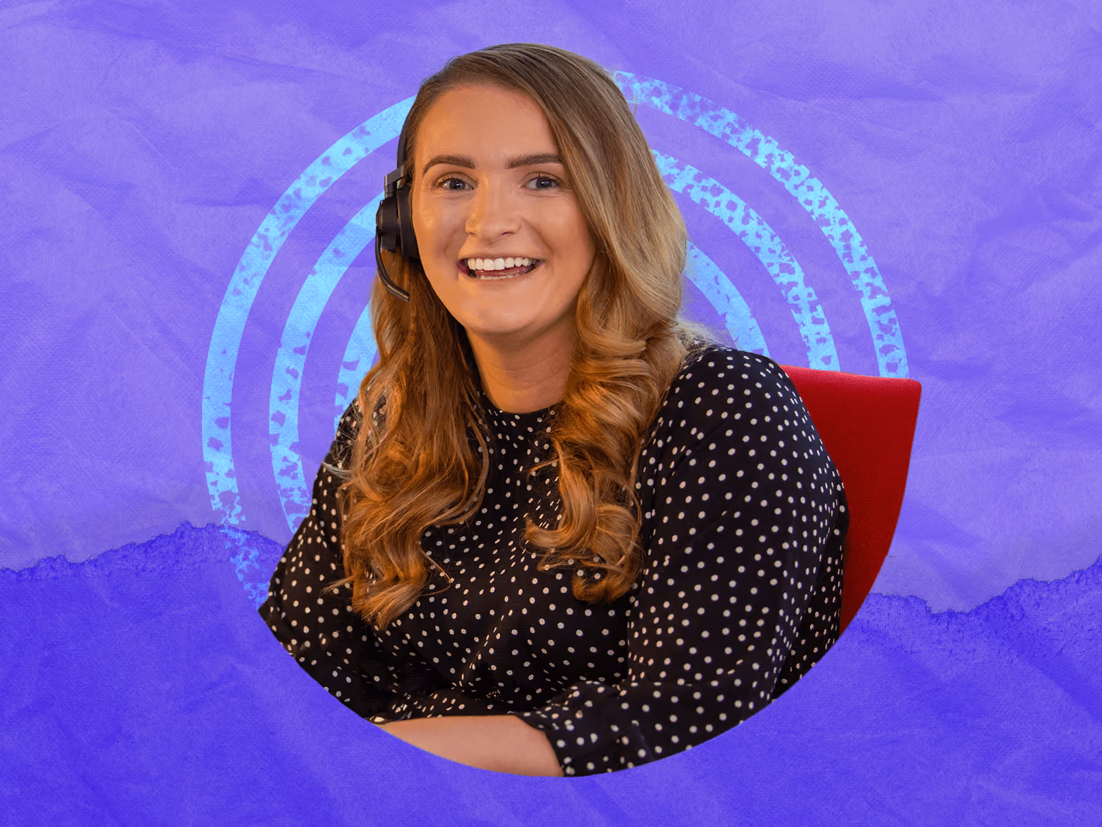 Smiling woman with headset and wavy hair sitting on a red chair against a purple background.