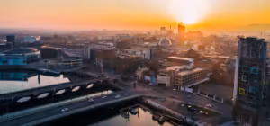 Cityscape with buildings, roads, a river, and sunset casting a warm glow over the skyline.