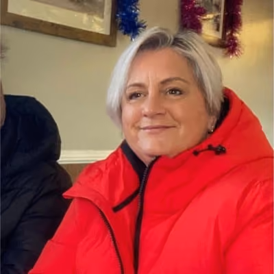 Smiling woman with short gray hair wearing a bright red jacket sitting indoors with holiday decorations.