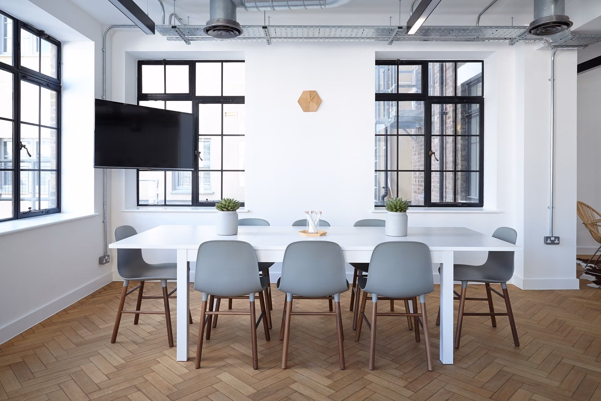 Modern office meeting room with white table, eight gray chairs, two potted plants, and large windows.
