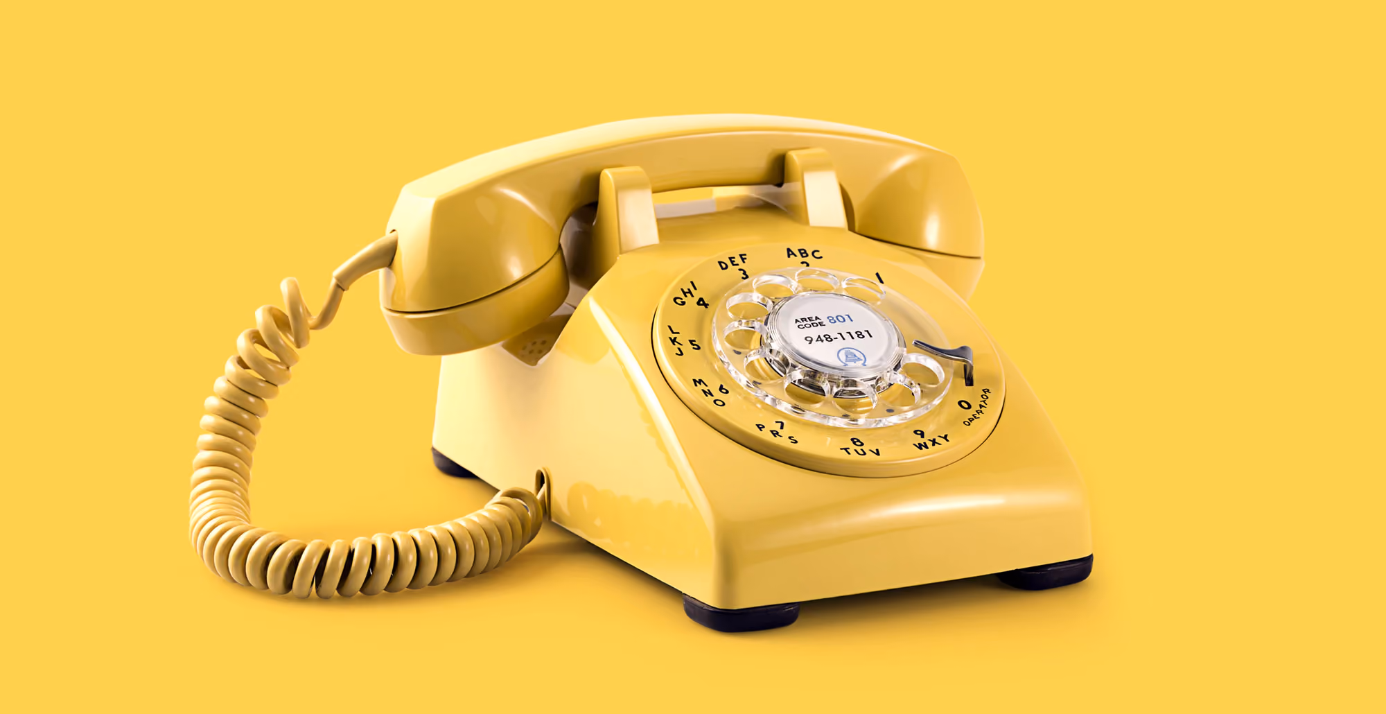 Yellow rotary dial telephone with coiled cord on a yellow background.