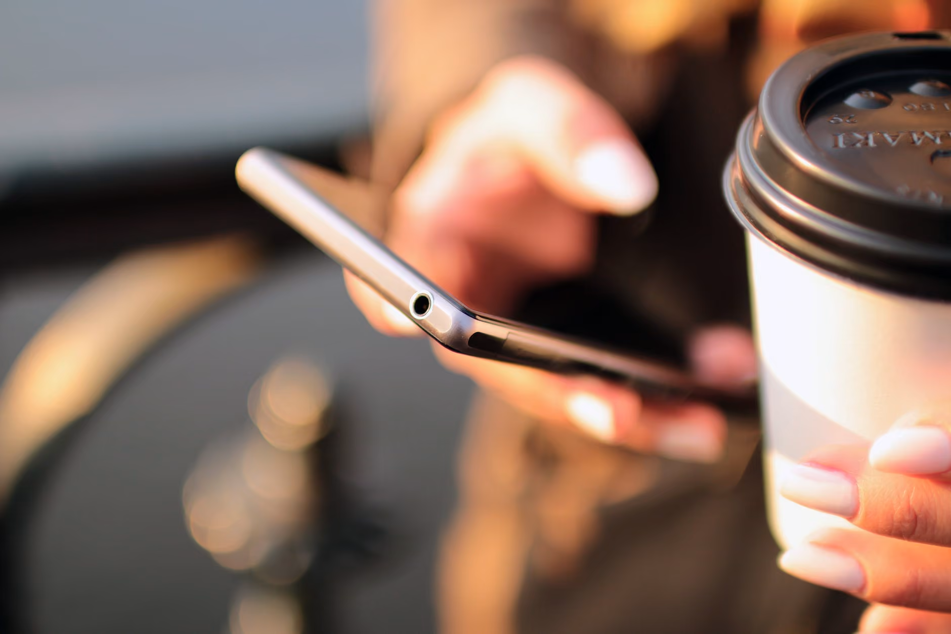 Close-up of hands holding a smartphone and a takeaway coffee cup with a black lid.