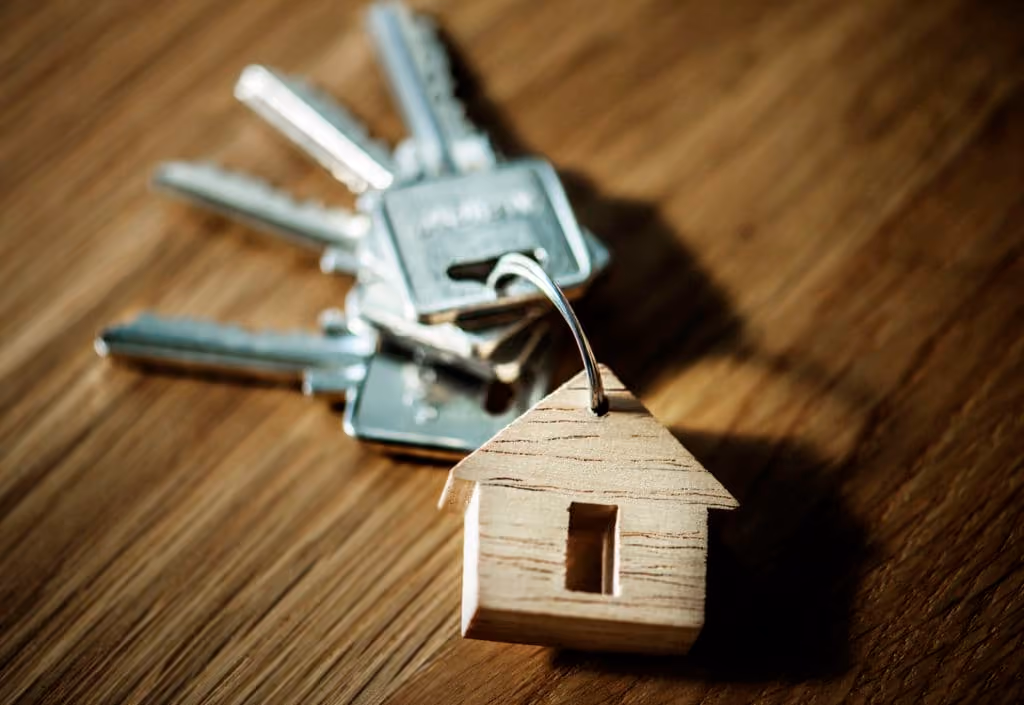 Silver keys on a wooden surface with a wooden house-shaped keychain.