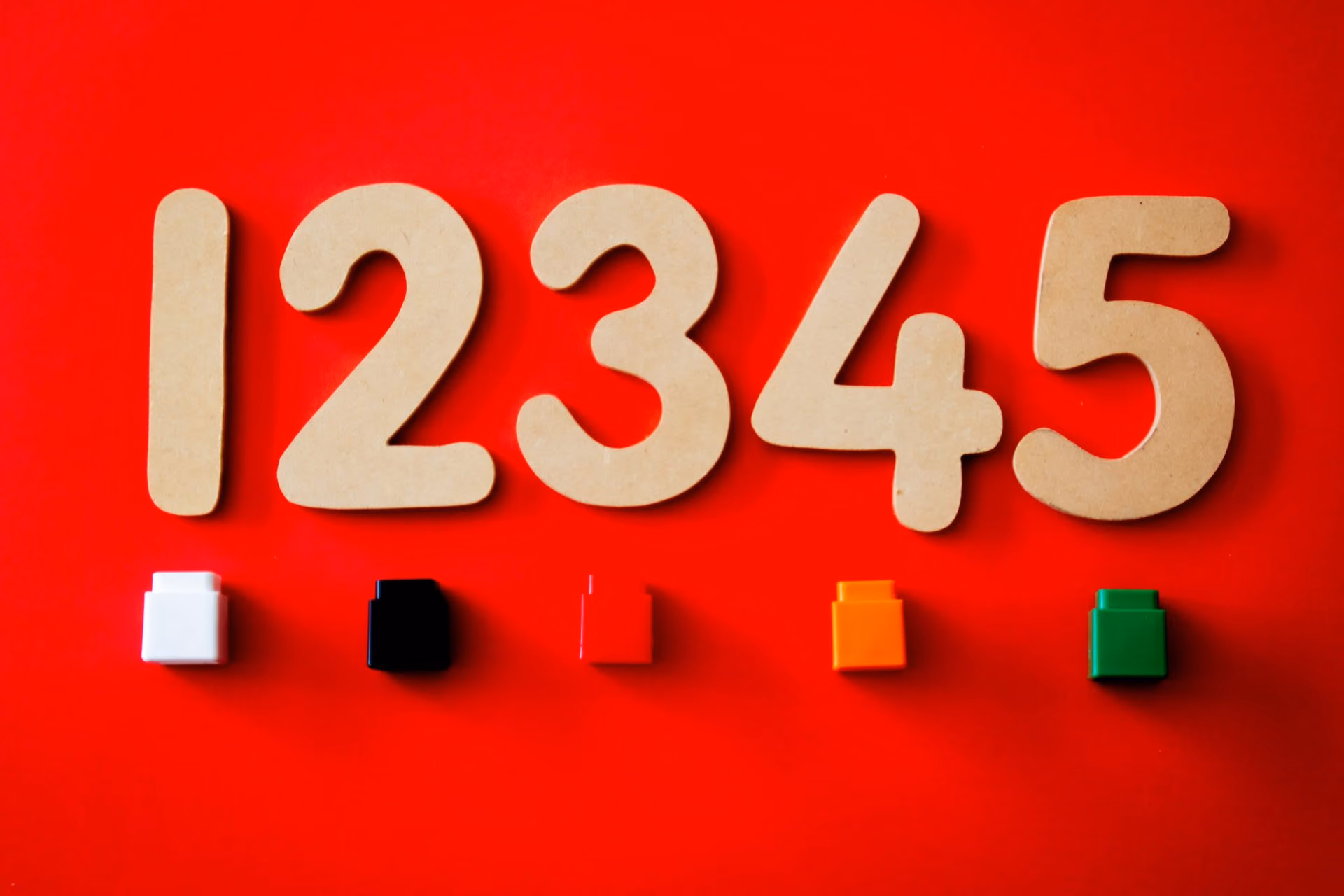 Numbers one to five in beige wood above blocks in white, black, red, orange, and green on red background.
