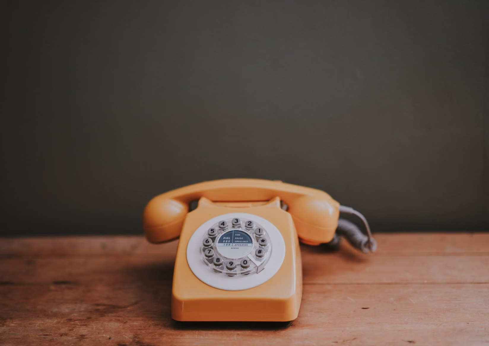 Vintage yellow rotary dial telephone on a wooden surface with a dark background.