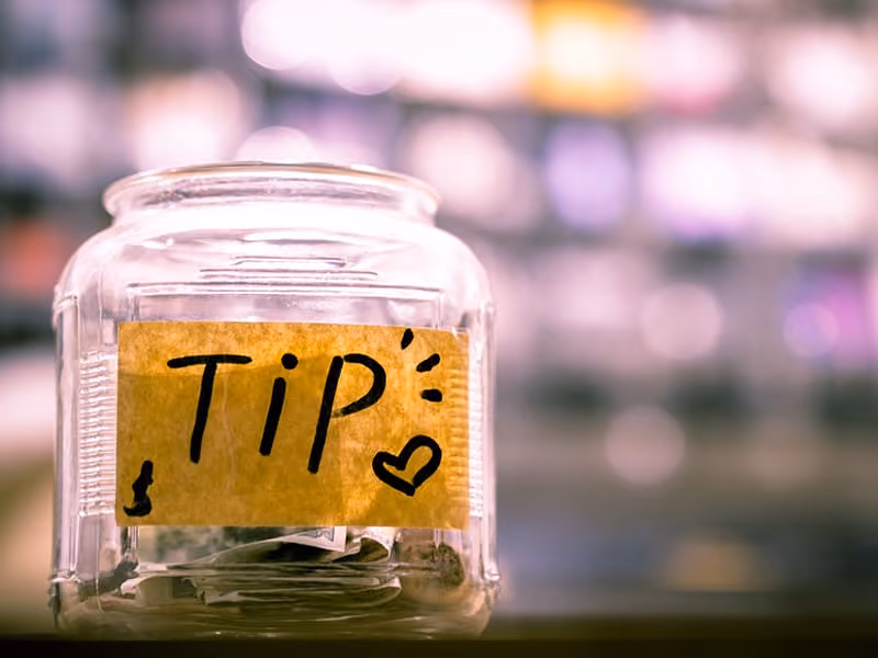 Glass tip jar with a yellow sticky note labeled 'TIP' and some bills inside.