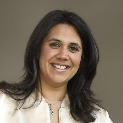 Smiling woman with layered dark hair wearing a light-colored jacket against a plain background.