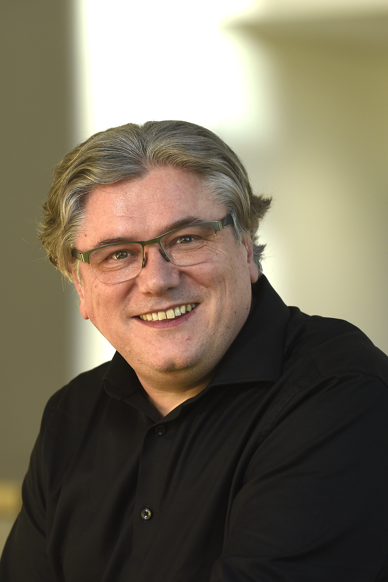 Smiling middle-aged man with gray hair and glasses wearing a black button-up shirt.