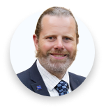 Smiling man with beard and tied-back hair wearing a suit and patterned tie in a circular frame.